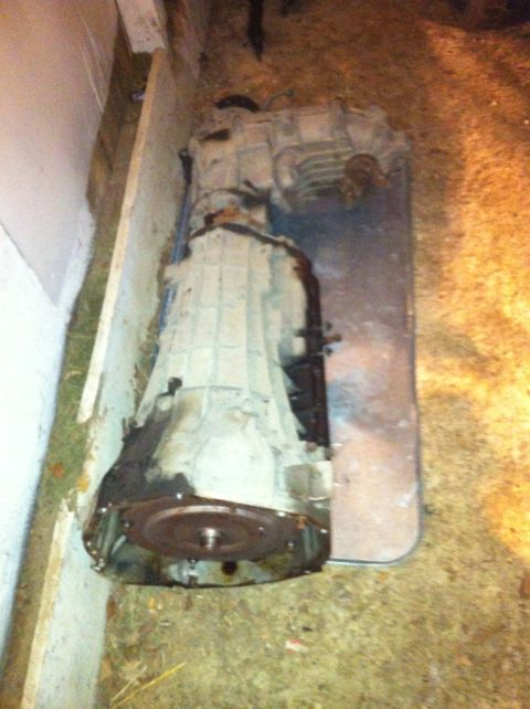 1996 Ford Bronco - A transmission assembly is shown resting on a metal sheet on the ground.