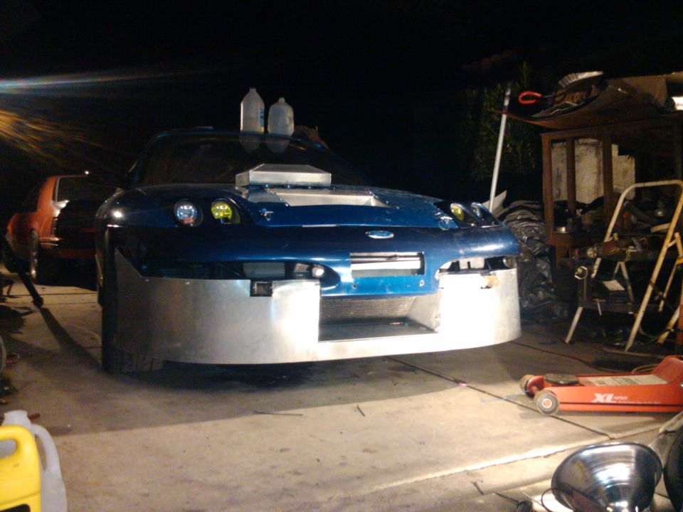 Blue car with large custom aluminum front bumper and hood scoop, parked in a garage