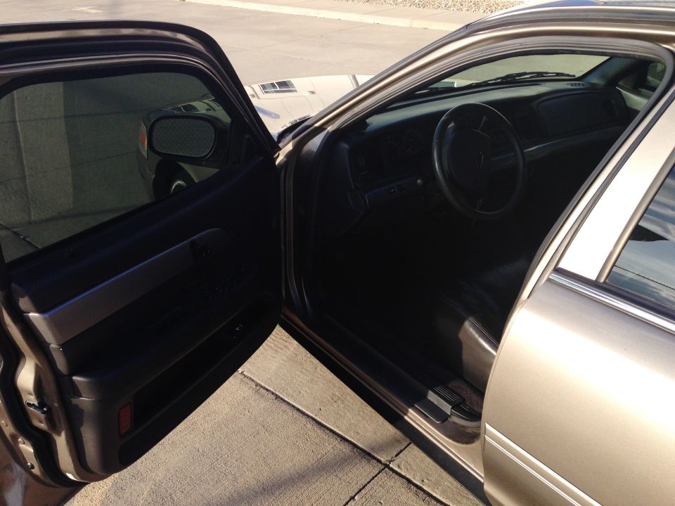 Open driver's door of tan sedan showing dark interior and dash