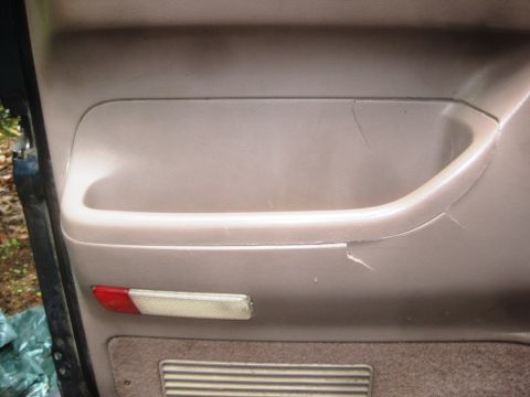 1993 Ford Bronco - Close-up of a worn interior door panel, showing damage to the armrest and a reflector light.