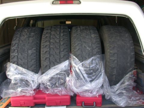 1994 Ford Bronco - Four tires are stored in the cargo area of a vehicle, resting on red toolboxes.