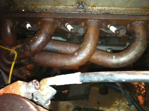1992 Ford Bronco - Close-up view of a rusty engine exhaust manifold and spark plugs, with a yellow wire and part of a bar visible.