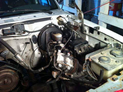 1992 Ford Bronco - The engine bay of a white 1992 Ford Bronco shows the air conditioning compressor and brake fluid reservoir.