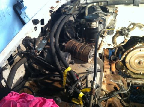 1992 Ford Bronco - Close-up view of a vehicle's engine bay, showing various hoses, a black canister, and rusty parts.