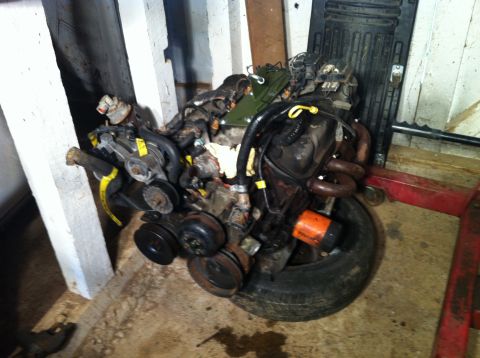 1992 Ford Bronco - Engine assembly resting on a tire, an orange oil filter and various hoses and belts.