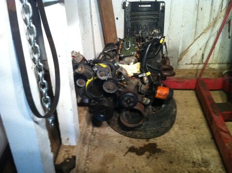 1992 Ford Bronco - An engine assembly rests on a tire in a workshop setting, with chains and a red engine hoist visible.
