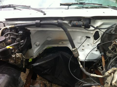1992 Ford Bronco - The engine bay of a white vehicle shows exposed hoses and wiring, with a black tarp obscuring some components.