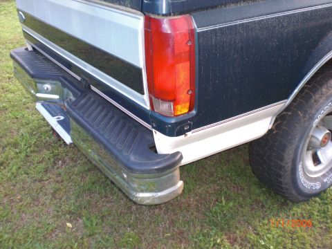 1993 Ford Bronco - Rear view of a dark green and white pickup truck, showing the bumper and taillight.