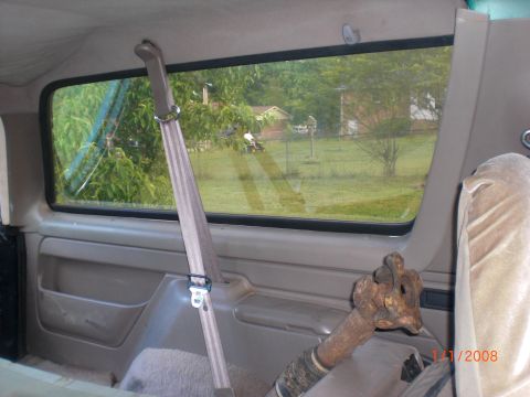1993 Ford Bronco - The interior of a vehicle is visible, a seatbelt and a rusty pipe, with a view of a rural landscape through the window.
