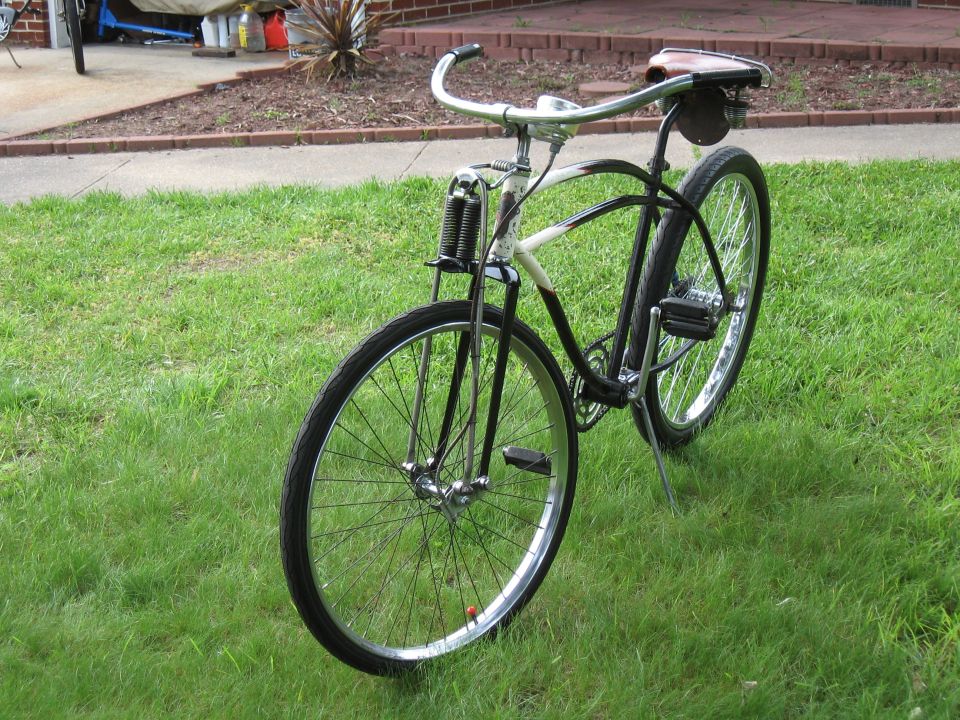 Front view of a vintage black and white bicycle with a brown leather seat and chrome handlebars, parked on grass