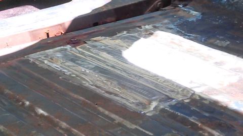 1979 Ford Bronco - Close-up of a rusted metal floor pan showing repair work with welds and filler.