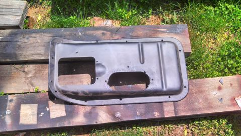 1979 Ford Bronco - A black metal door panel with two large cutouts rests on wooden planks outdoors.
