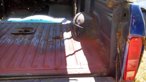 1979 Ford Bronco - The rear of a 1979 Ford Bronco shows a worn truck bed with visible rust and primer.