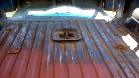1979 Ford Bronco - The interior floor of a vehicle shows ribbed metal construction and a central tie-down anchor, indicating a utilitarian design.