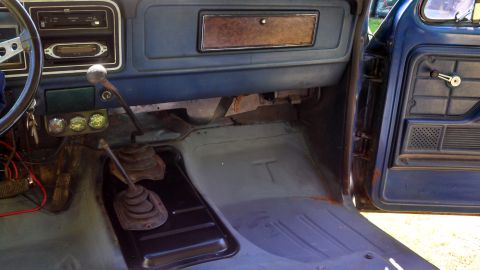 1979 Ford Bronco - The interior of a blue truck shows the dashboard, steering wheel, floor, and door panel with two gear shifters.