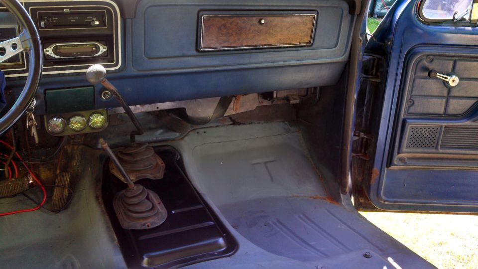 Interior of a blue truck, showing the dashboard, steering wheel, floor, and door panel. Two gear shifters are visible