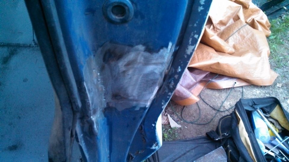 Blue vehicle door frame with body filler and rust, next to a tarp and tool bag