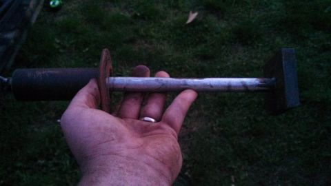 1979 Ford Bronco - A hand holds a metal tool, possibly for automotive repair, outdoors.