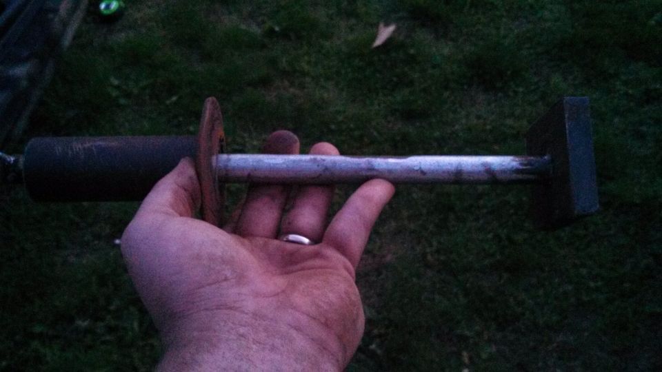 Hand holding a metal tool with a cylindrical end and a rectangular block on the other end