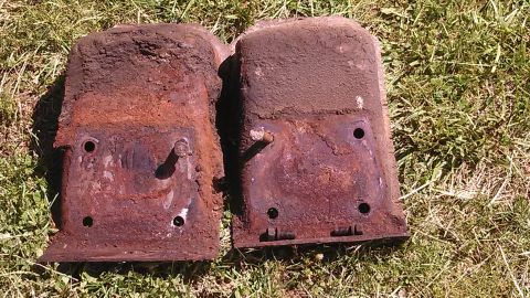 1979 Ford Bronco - Two heavily rusted metal parts are shown on a grassy surface, with visible bolt holes and mounting points.