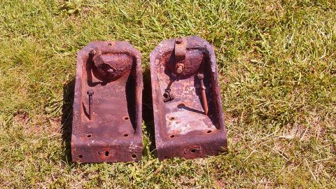 1979 Ford Bronco - Two heavily rusted metal brackets lie on a grassy surface.