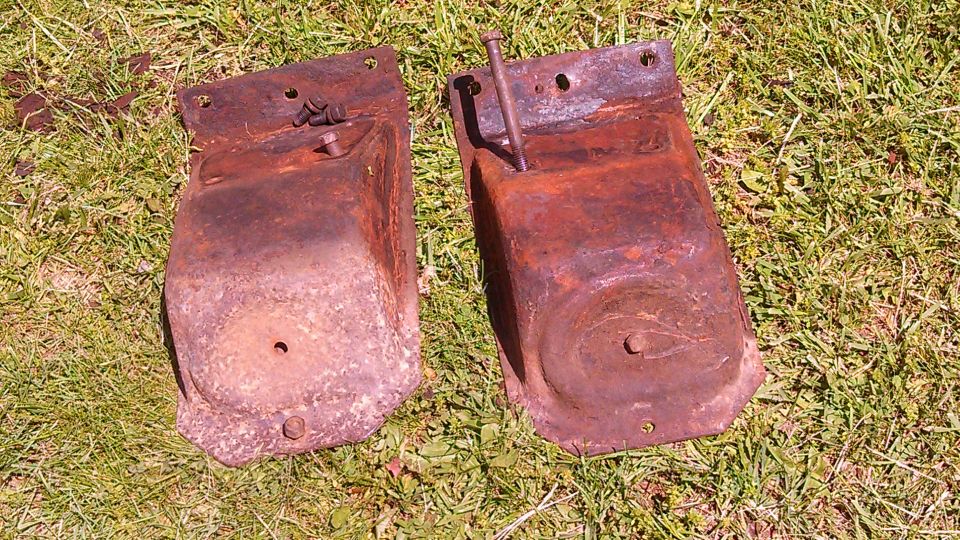 Two heavily rusted metal brackets with bolts, lying on grass