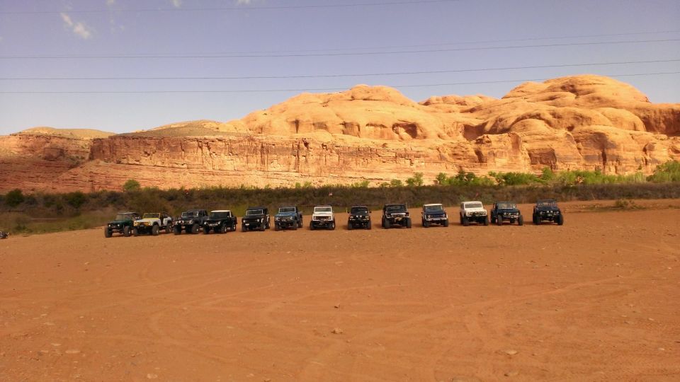 Multiple SUVs parked in a row on a dirt road with red rock formations in the background