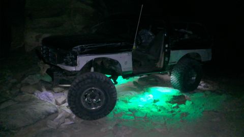 1994 Ford Bronco - Modified 1994 Ford Bronco with custom wheels and green underglow lights, seen off-road at night.