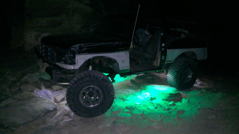 1994 Ford Bronco with custom modifications and green underglow lights, parked on rocks at night