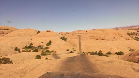 1994 Ford Bronco - A dark SUV navigates a dirt road through a vast desert landscape under a clear blue sky.