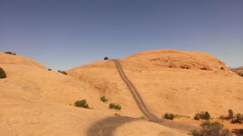 1994 Ford Bronco - Vehicle navigates a challenging off-road path on a sun-drenched rocky landscape.