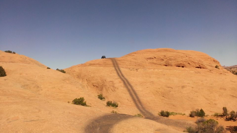Off-road vehicle on a dirt track ascending a rocky hill under a clear blue sky