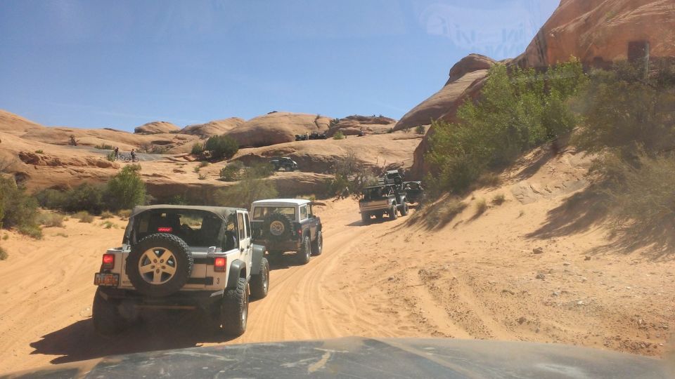 Several Jeeps driving on a sandy desert trail with red rock formations