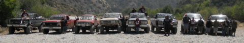 1986 Ford Bronco - A group of off-road vehicles are lined up in a natural setting, with several people present.