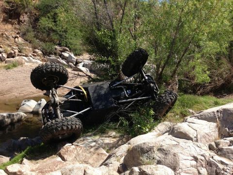 1966 Ford Bronco - An off-road vehicle has overturned in a rocky stream bed, surrounded by vegetation and rocks.