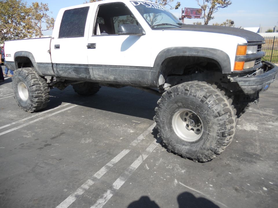 White 1995 Chevrolet C/K pickup truck with lifted suspension and oversized off-road tires, parked in a lot