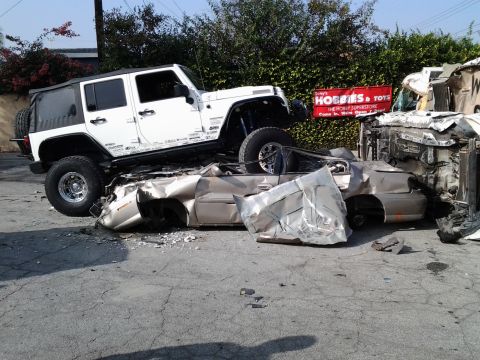 1986 Ford Bronco - A collision scene shows a white Jeep resting on a severely damaged sedan, with another vehicle also wrecked nearby.