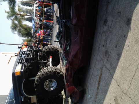 1986 Ford Bronco - A heavily modified truck with large tires is parked next to a damaged car, with onlookers gathered in the background.