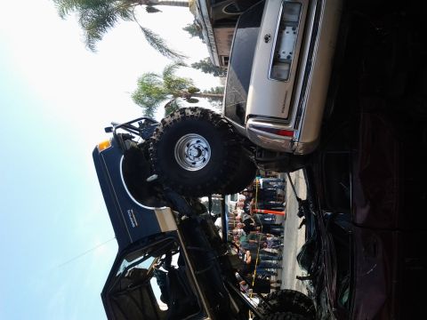 1986 Ford Bronco - A heavily modified 1986 Ford Bronco, lifted with large tires and a roll cage, is seen with a beige sedan precariously balanced on its roof.