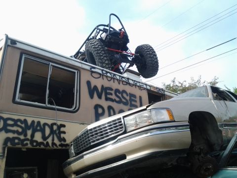 1986 Ford Bronco - An RV and a car are parked together, with a buggy loaded onto the RV's roof. Graffiti covers the side of the RV.