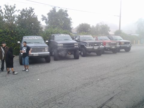 1986 Ford Bronco - A group of modified trucks and SUVs are parked together on a foggy day.