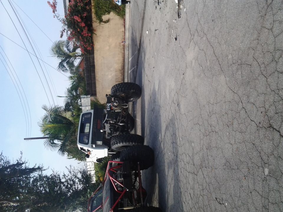 two modified off-road trucks, one white, one red, parked on pavement
