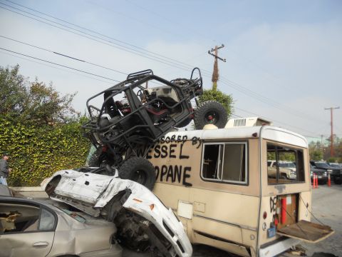 1986 Ford Bronco - A chaotic scene unfolds as an off-road buggy is precariously balanced on a bus, with several cars crushed beneath.