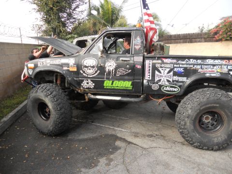 1986 Ford Bronco - This heavily modified Toyota pickup truck features oversized tires and numerous decals, with its hood open for engine work.