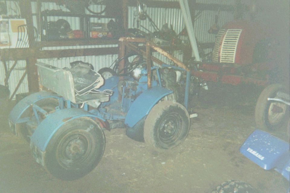 Blue tractor with a roll cage and a red tractor in the background