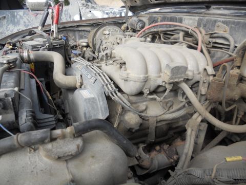 1986 Ford Bronco - Jumper cables are connected to the battery in this dusty engine bay, showing a 2400 FourCam engine.