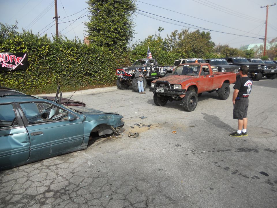 Orange pickup truck with a rusty front end and large tires parked on cracked asphalt