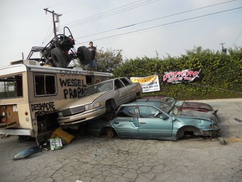 1986 Ford Bronco - A collection of damaged vehicles are piled up, with a buggy mounted on top of a bus.