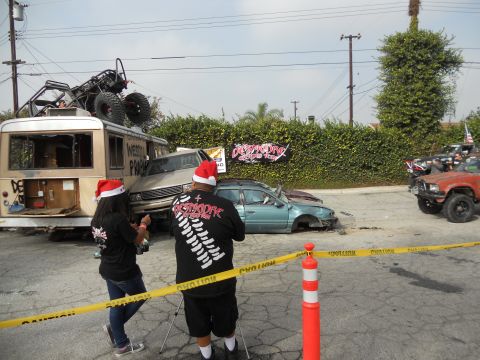 1986 Ford Bronco - Several damaged vehicles and a bus are present, with people wearing Santa hats observing the scene.