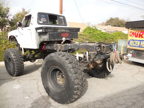 1986 Ford Bronco - This modified pickup truck chassis features massive off-road tires and a rear-mounted toolbox, suggesting custom modifications.